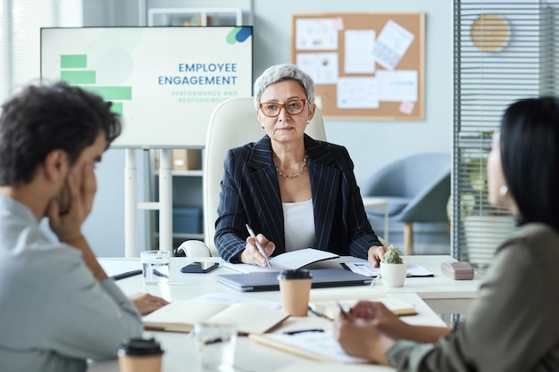 Femme d'affaires senior assise à la tête de la table lors d'une réunion d'affaires avec l'équipe