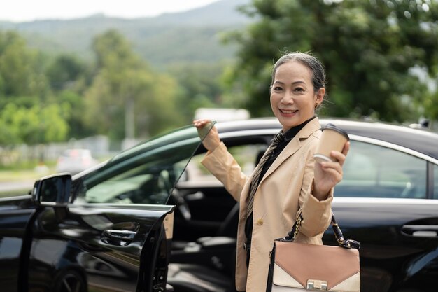 Femme d'affaires senior confiante débarquant de la voiture de luxe avec un regard souriant devant la caméra