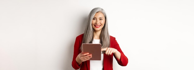 Femme d'affaires senior souriante à l'aide d'une tablette numérique pointant le doigt sur l'écran debout sur w