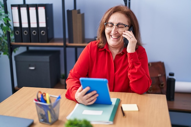 Femme d'affaires senior utilisant un pavé tactile parlant sur un smartphone au bureau