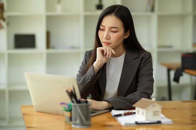 Femme d'affaires sérieuse avec la main sur le menton assise et travaillant sur la pensée pensive d'un ordinateur portable