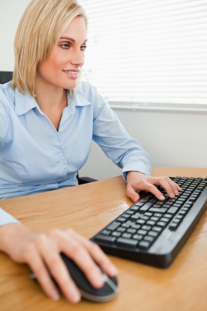 Femme d&#39;affaires souriant avec les mains sur la souris et le clavier en regardant l&#39;écran