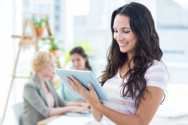 Femme d&#39;affaires souriant en utilisant une tablette avec des collègues