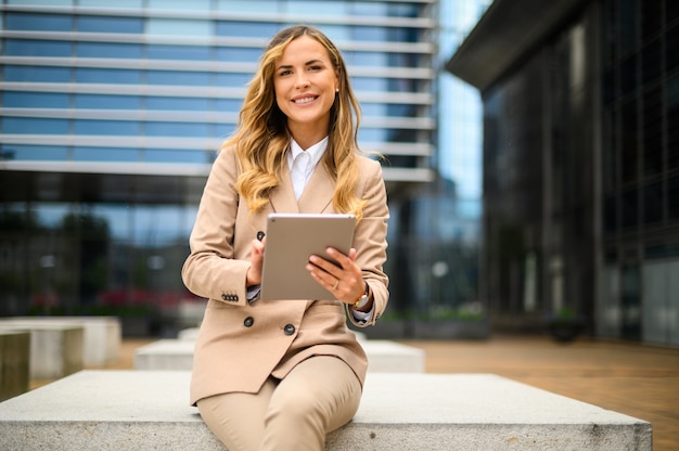 Femme d'affaires souriante à l'aide d'une tablette numérique en plein air