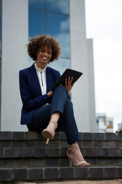 Femme d'affaires souriante à l'aide de tablette numérique près d'un immeuble de bureaux