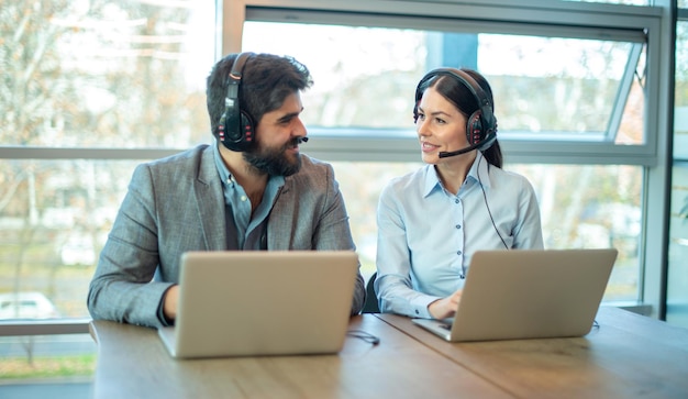Une femme d'affaires souriante et un bel homme d'affaires en casque utilisant des ordinateurs portables tout en travaillant au bureau