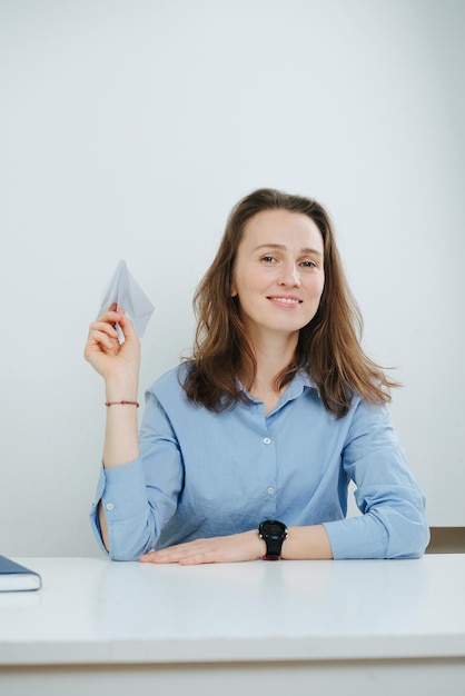 Femme d'affaires souriante en chemise bleue avec un avion en papier à la main