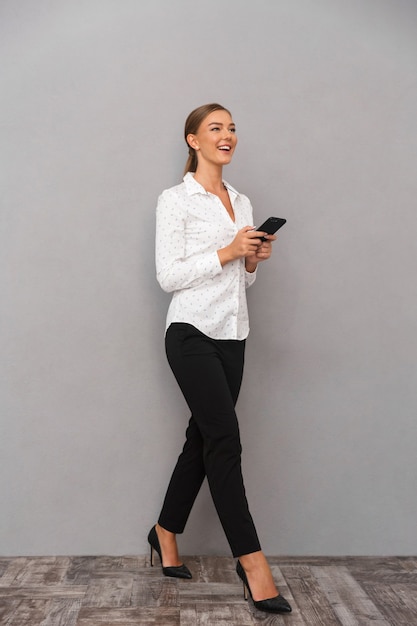 Femme d'affaires souriante sur fond de mur gris à l'aide d'un téléphone portable.