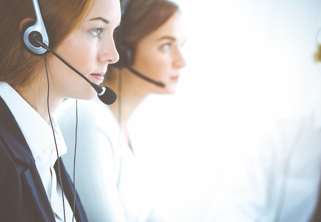 Femme d'affaires souriante et joyeuse avec un casque consultant les clients. Groupe d'opérateurs téléphoniques divers au travail dans un bureau ensoleillé. Concept de centre d'appels et de gens d'affaires.