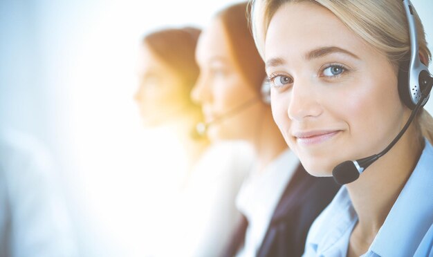 Femme d'affaires souriante et joyeuse avec un casque consultant les clients. Groupe d'opérateurs téléphoniques divers au travail dans un bureau ensoleillé. Concept de centre d'appels et de gens d'affaires.