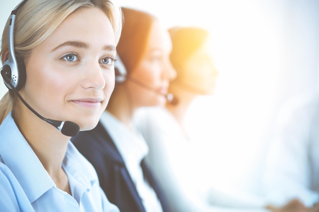 Femme d'affaires souriante et joyeuse avec un casque consultant les clients. Groupe d'opérateurs téléphoniques divers au travail dans un bureau ensoleillé. Concept de centre d'appels et de gens d'affaires.