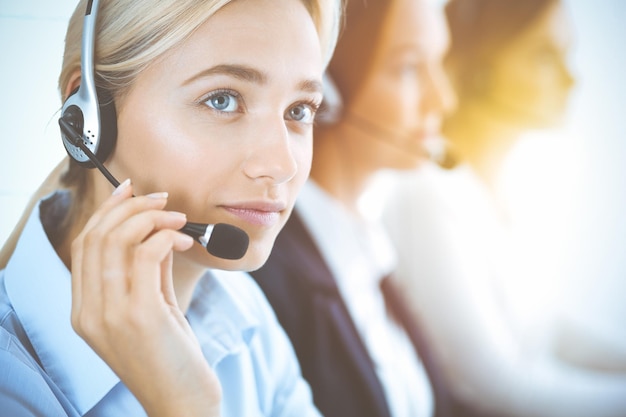 Femme d'affaires souriante et joyeuse avec un casque consultant les clients. Groupe d'opérateurs téléphoniques divers au travail dans un bureau ensoleillé. Concept de centre d'appels et de gens d'affaires.