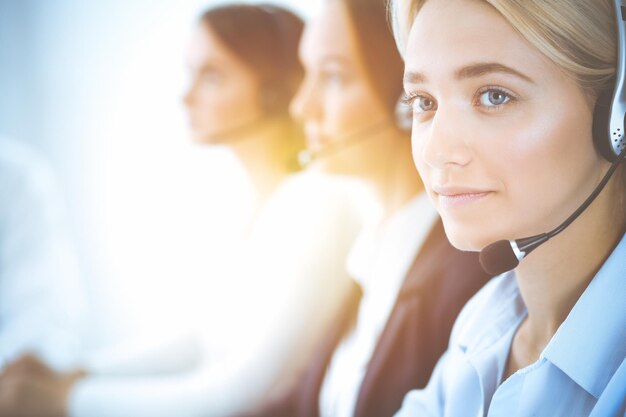 Femme d'affaires souriante et joyeuse avec un casque consultant les clients. Groupe d'opérateurs téléphoniques divers au travail dans un bureau ensoleillé. Concept de centre d'appels et de gens d'affaires.