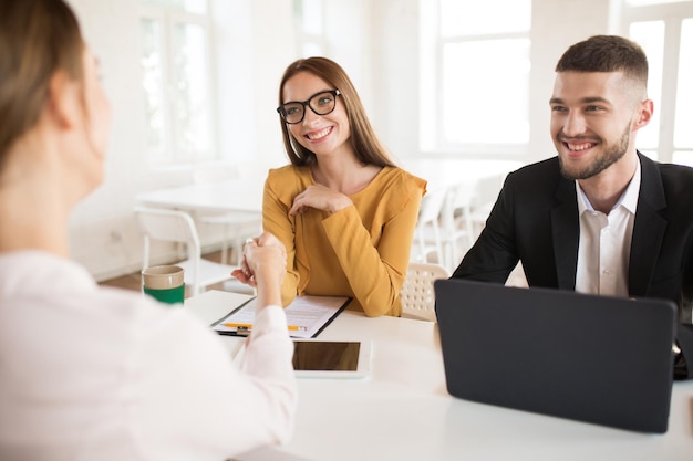 Femme d'affaires souriante à lunettes serrant joyeusement la main du candidat avec un homme d'affaires près de Jeunes employeurs joyeux passant un entretien d'embauche dans un bureau moderne