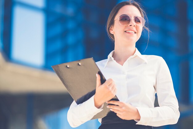 La femme d'affaires souriante en lunettes de soleil se tient avec une tablette