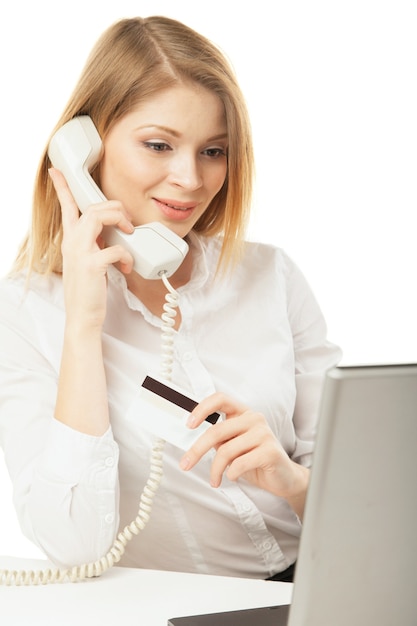 Femme d'affaires souriante avec ordinateur portable, carte de crédit et téléphone sur fond blanc