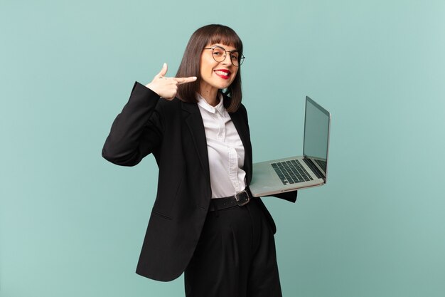 Femme d'affaires souriante pointant avec confiance vers son propre large sourire, attitude positive, détendue et satisfaite