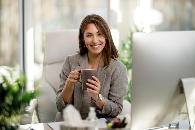 Une femme d'affaires souriante qui réussit en dégustant une tasse de café au bureau. Regarder la caméra.