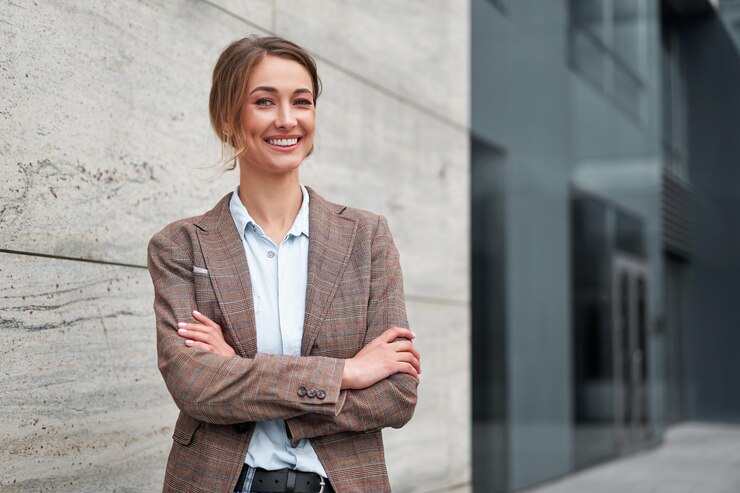 Une femme d'affaires souriante se tient les bras croisés devant un immeuble de bureaux.
