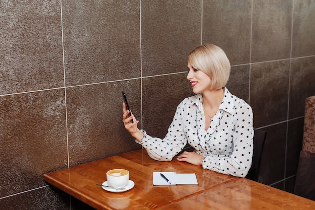 Femme d'affaires souriante avec smartphone au café
