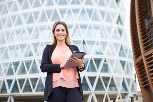 Femme d'affaires souriante tenant une tablette numérique en milieu urbain