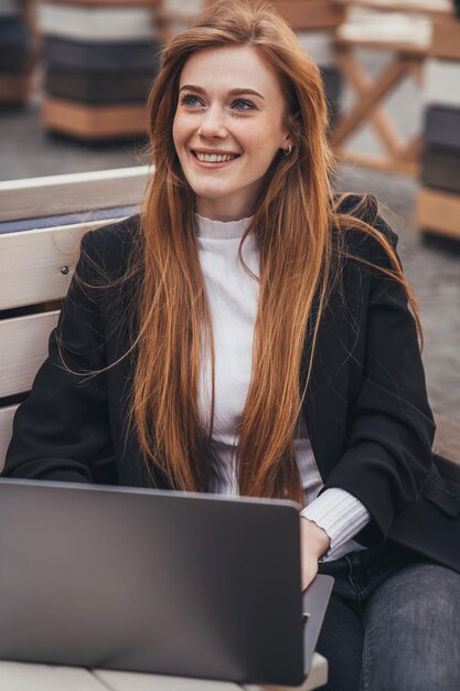 Femme d'affaires souriante travaillant sur pc à l'air frais assis dehors sur un banc dans le parc de la ville Belle jeune fille Technologie moderne Portrait d'entreprise Technologie de marketing