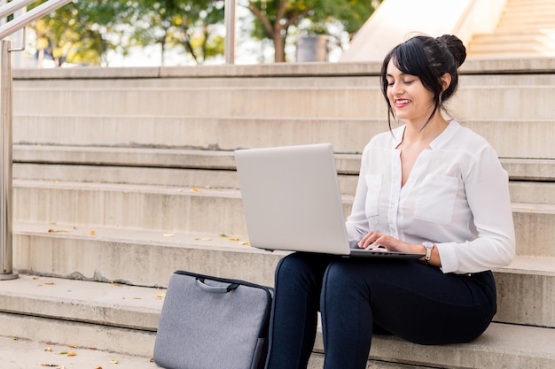 Femme d'affaires souriante travaillant sur son ordinateur portable assis sur un escalier en béton, concept d'entrepreneur numérique et mode de vie urbain, espace de copie pour le texte