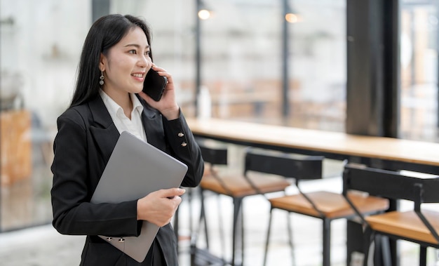 Femme d'affaires souriante utilisant un téléphone au bureau Entrepreneur de petite entreprise regardant à l'extérieur et souriant