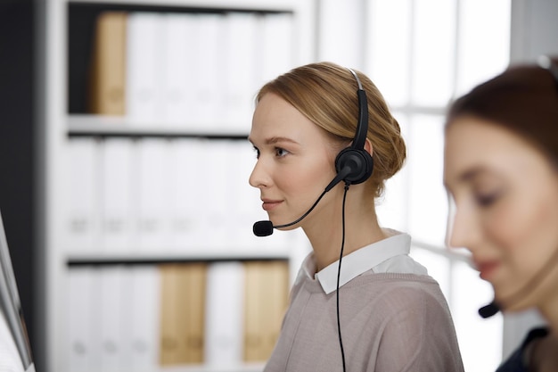 Femme d'affaires sympathique parlant par casque au bureau. Centre d'appels et groupe de personnes diversifié en affaires.