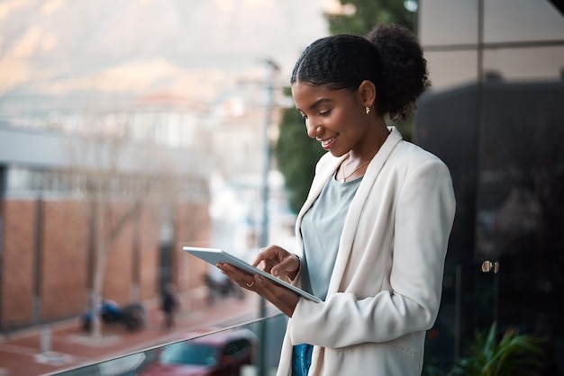 Femme d'affaires sur une tablette numérique à l'extérieur d'un bureau moderne seule Employée souriante regardant des publications sur le Web et les médias sociaux sur un balcon Employée sur un appareil à écran tactile avec espace de copie
