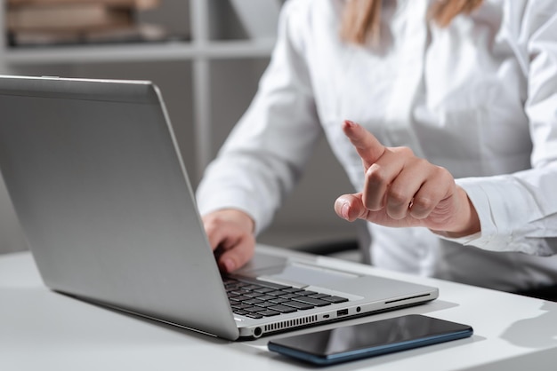 Femme d'affaires tapant les mises à jour récentes sur le clavier de l'ordinateur portable sur le bureau avec téléphone portable et pointant