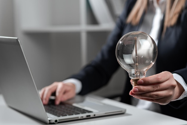 Femme d'affaires tapant des mises à jour récentes sur ordinateur portable sur le bureau tenant une ampoule