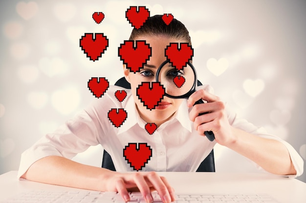 Femme d'affaires tapant et regardant à travers une loupe contre la conception du coeur de la Saint-Valentin