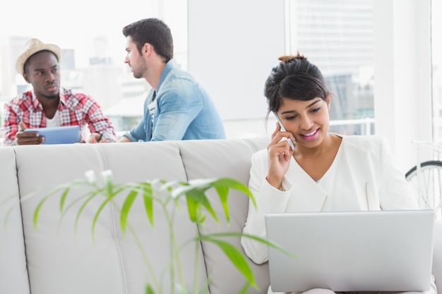 Femme d&#39;affaires téléphonant et en utilisant un ordinateur portable sur le canapé