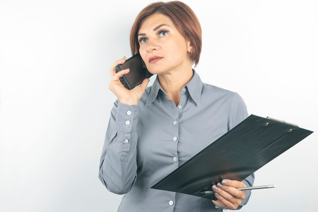 Femme d'affaires avec téléphone et documents en mains sur un mur blanc.