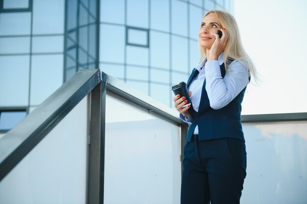 Femme d'affaires avec téléphone près du bureau Portrait de belle femme souriante dans des vêtements de bureau de mode parlant au téléphone tout en se tenant à l'extérieur