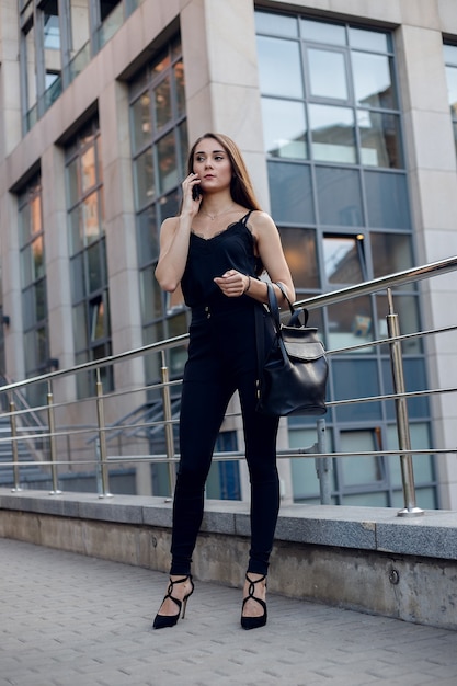 Femme D'affaires Avec Téléphone Près Du Bureau. Portrait de belle femme souriante dans des vêtements de bureau de mode, parler au téléphone tout en se tenant à l'extérieur. Communication téléphonique. Image de haute qualité.