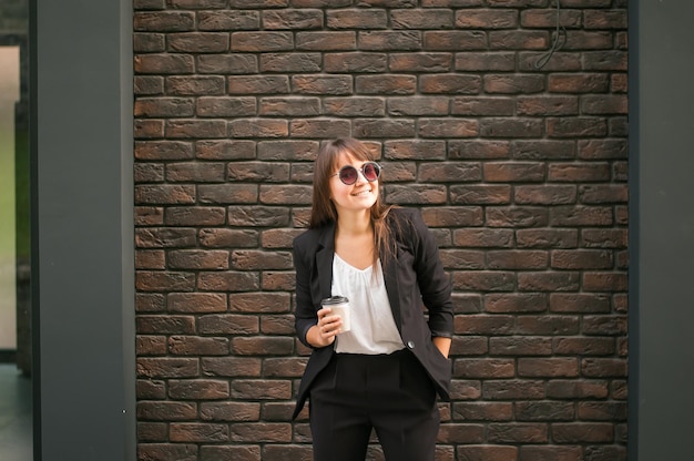 femme d'affaires tenant un café à la main près d'un mur de briques