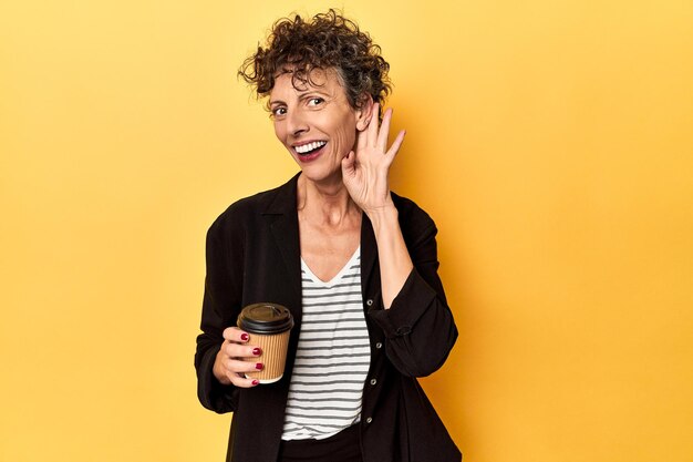 Femme d'affaires tenant du café à emporter sur jaune essayant d'écouter des potins