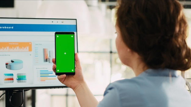 Une femme d'affaires tenant un écran vert sur son téléphone et travaillant sur le développement du marketing au bureau de l'agence. Un employé de l'entreprise utilisant un modèle de chromakey et un espace de copie isolé en affichage.