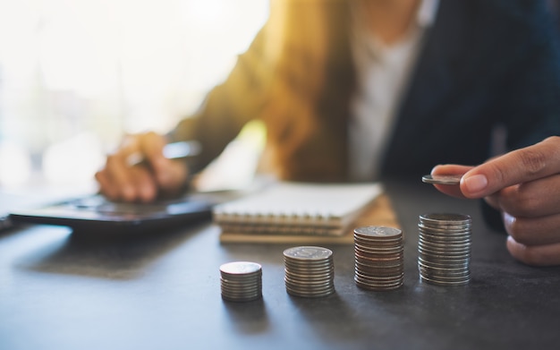 Femme D'affaires Tenant Et Empilant Des Pièces Tout En Calculant De L'argent Sur La Table