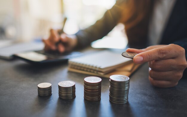 Femme d'affaires tenant et empilant des pièces tout en calculant de l'argent sur la table