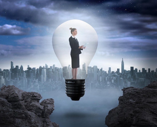 Femme d'affaires tenant une tablette dans une ampoule contre une grande ville à l'horizon