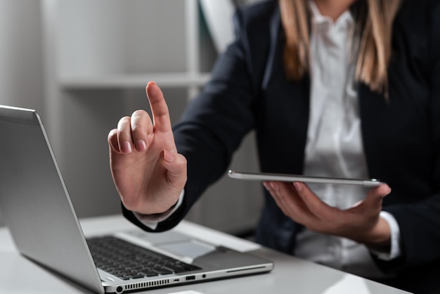 Femme d'affaires tenant la tablette dans une main et pointant sur des nouvelles importantes avec un doigt assis femme au bureau avec téléphone portable à la main présentant des informations