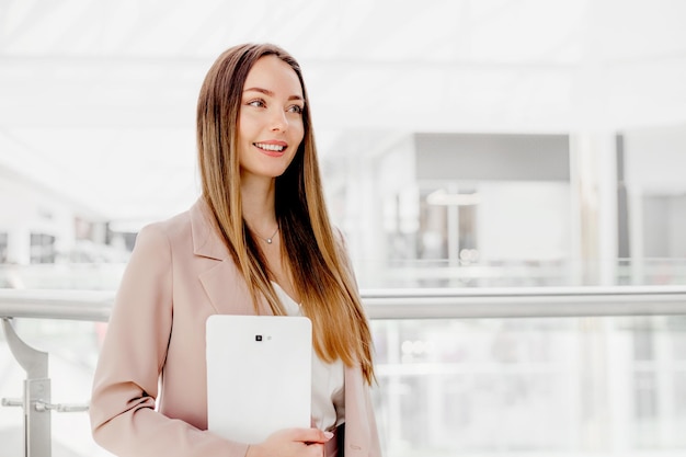 Femme d'affaires tenant une tablette numérique debout dans le centre d'affaires et regardant loin