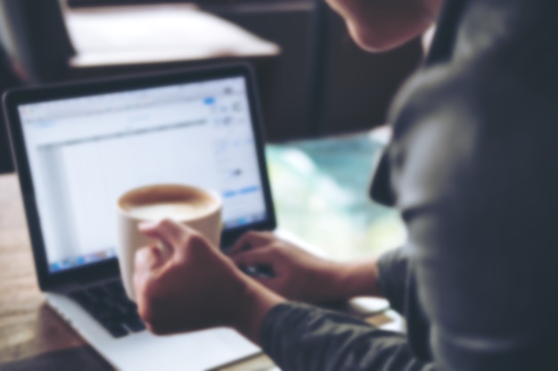 Une femme d&#39;affaires tenant une tasse de café tout en utilisant et en tapant sur un ordinateur portable