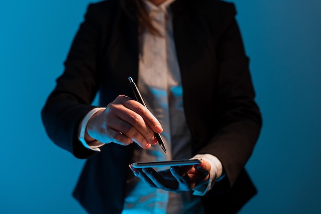 Femme d'affaires tenant un téléphone portable et pointant avec un stylo sur des messages importants Femme debout en costume ayant un téléphone portable et présentant des informations cruciales