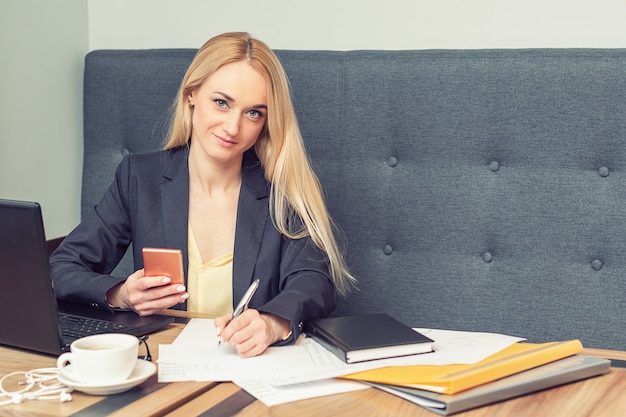 Femme d'affaires tient le smartphone et écrit sur un blanc au bureau