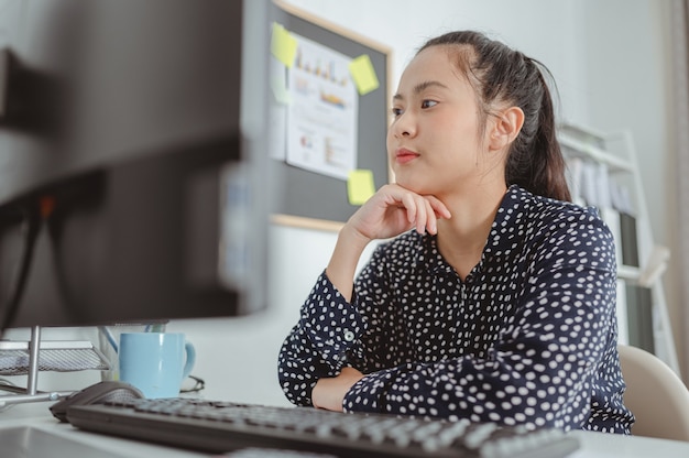 Femme d'affaires travaillant et assise au bureau au bureau en plaçant le menton sur ses mains et en détournant les yeux