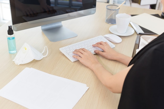 Une femme d'affaires travaillant dans un bureau et tapant sur un clavier avec un vaporisateur d'alcool